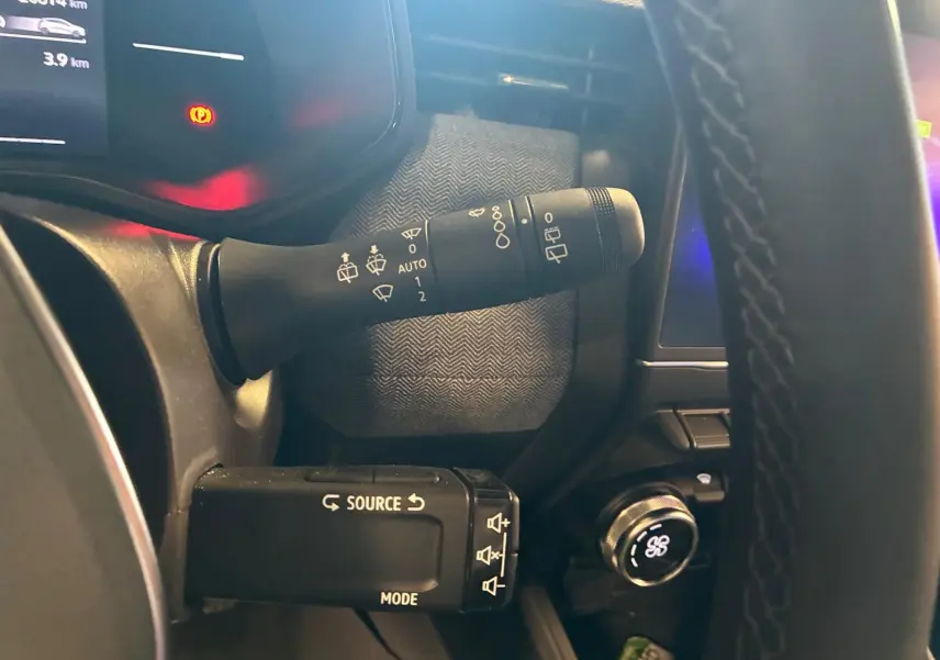 Gros plan sur la commande des essuie-glaces et du multimédia à gauche du volant d’une Renault Clio gris schiste, intérieur sombre.