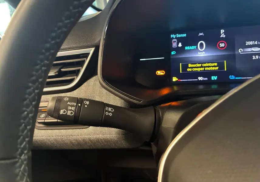 Détail du combiné d'instruments et commodo gauche dans l'habitacle gris noir de la Renault Clio hybride 2025.