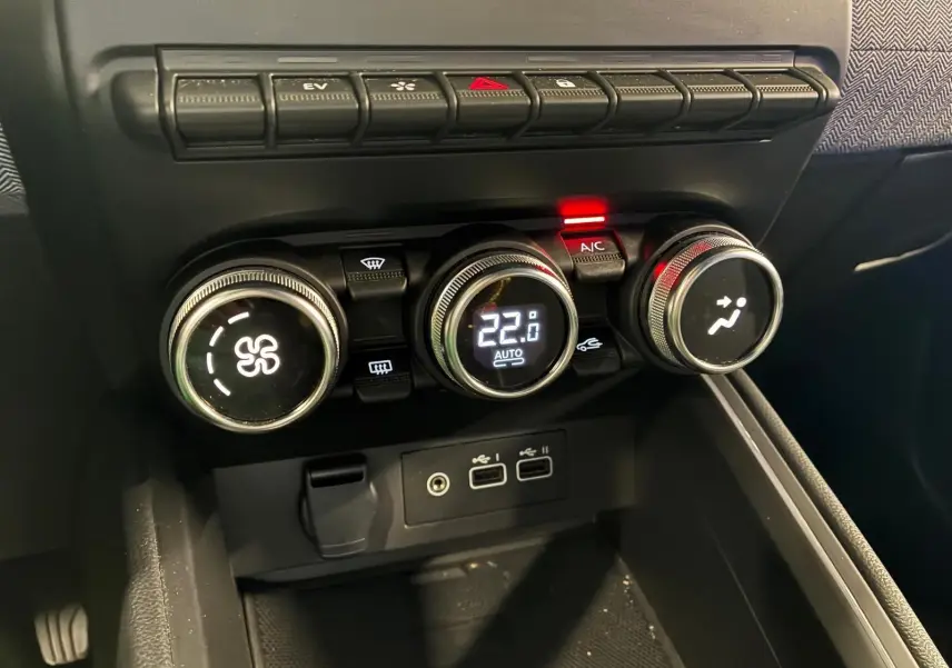 Gros plan sur la console centrale de la Renault Clio 2025, boutons de climatisation numériques et connectiques USB visibles.