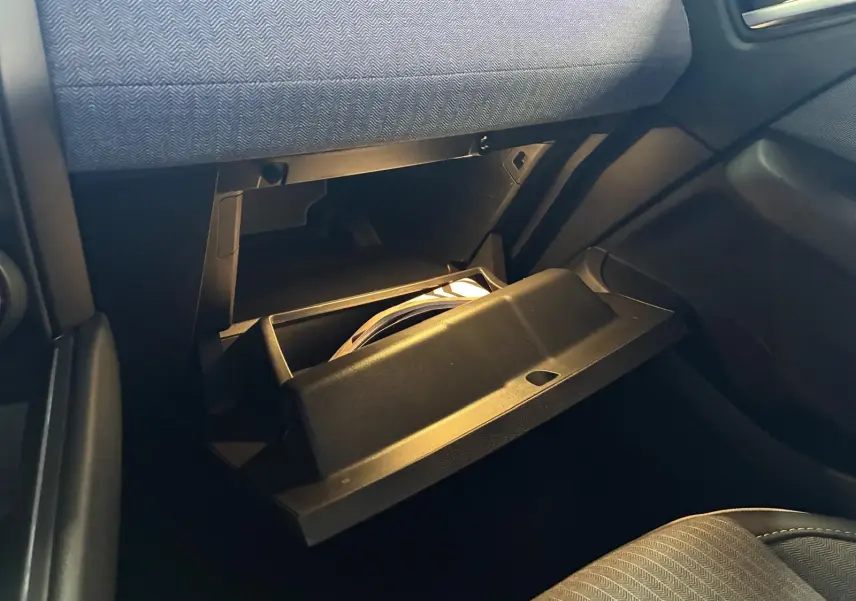 Gros plan sur la boîte à gants ouverte côté passager de la Renault Clio 2025, intérieur tissu gris noir.