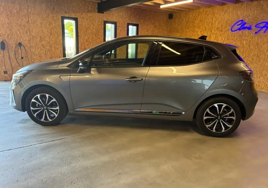 Profil droit d'une Renault Clio 2025 gris schiste, avec jantes alliage et vitres teintées, stationnée en intérieur.