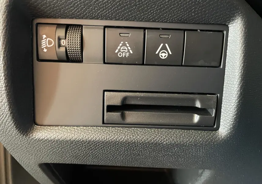 Gros plan sur les commandes noires du tableau de bord du Citroën C5 Aircross hybride 2025, avec réglage des phares et aides à la conduite.