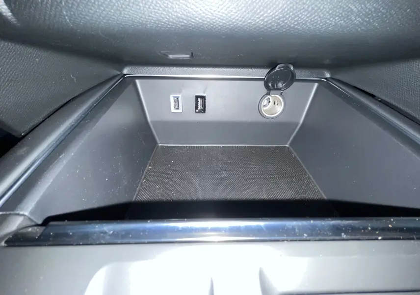 Gros plan de la prise 12V et ports USB dans le rangement central du Citroën C5 Aircross hybride blanc 2025.
