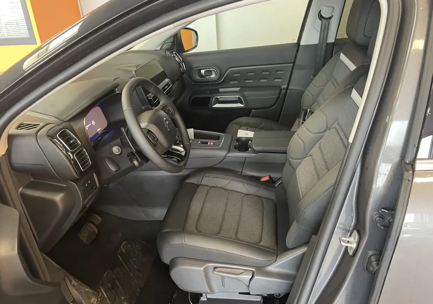 Vue intérieure côté conducteur du Citroën C5 Aircross hybride 2025, montrant sièges tissu/TEP gris et tableau de bord moderne.