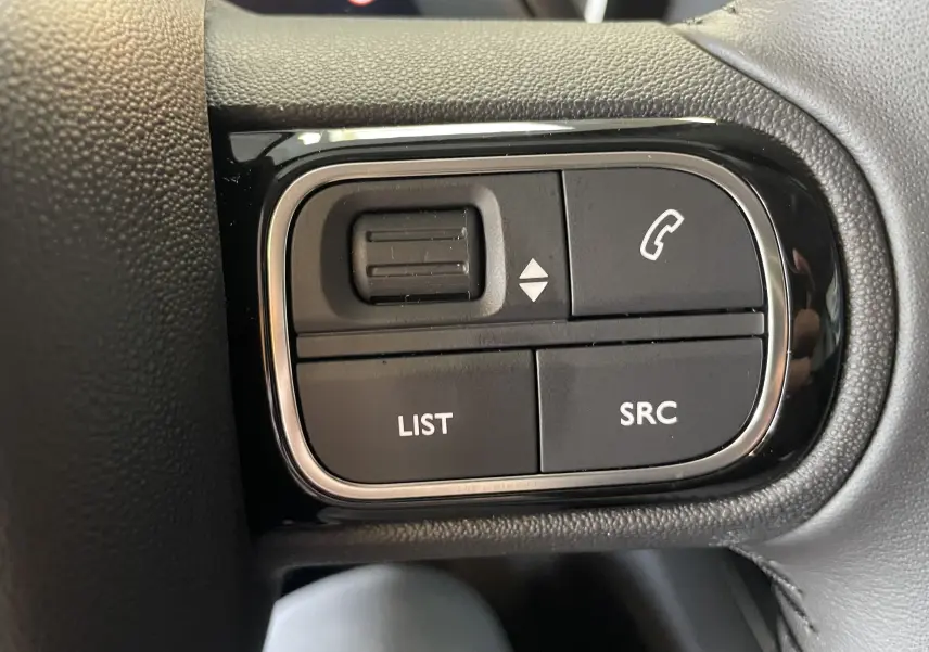 Gros plan sur les commandes au volant noir du Citroën C5 Aircross hybride 2025, boutons LIST et SRC visibles.