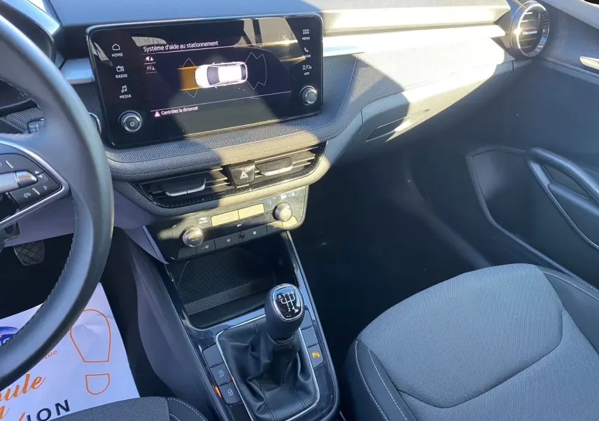 Intérieur avant droit d'une Skoda Fabia 2024 avec tableau de bord noir, écran tactile et levier de vitesse manuel.