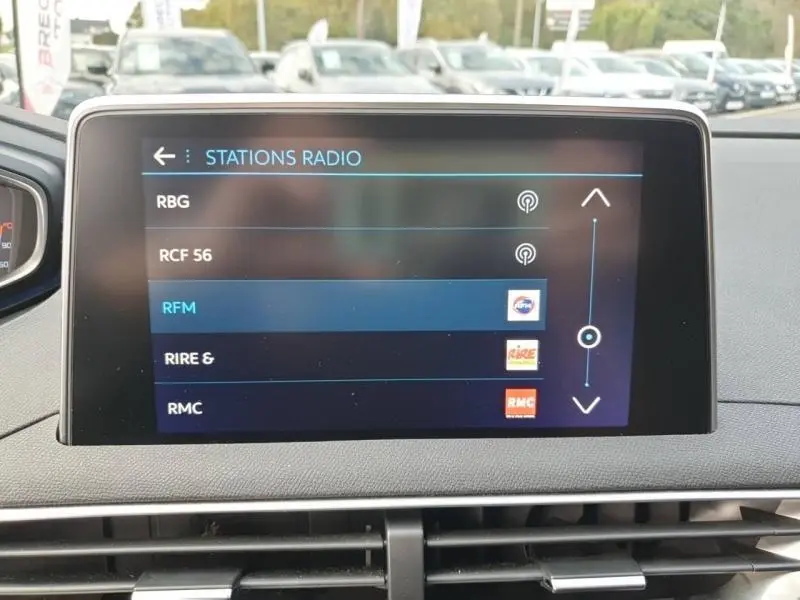 Écran tactile central du tableau de bord du Peugeot 3008 blanc nacré, affichant les stations radio disponibles.