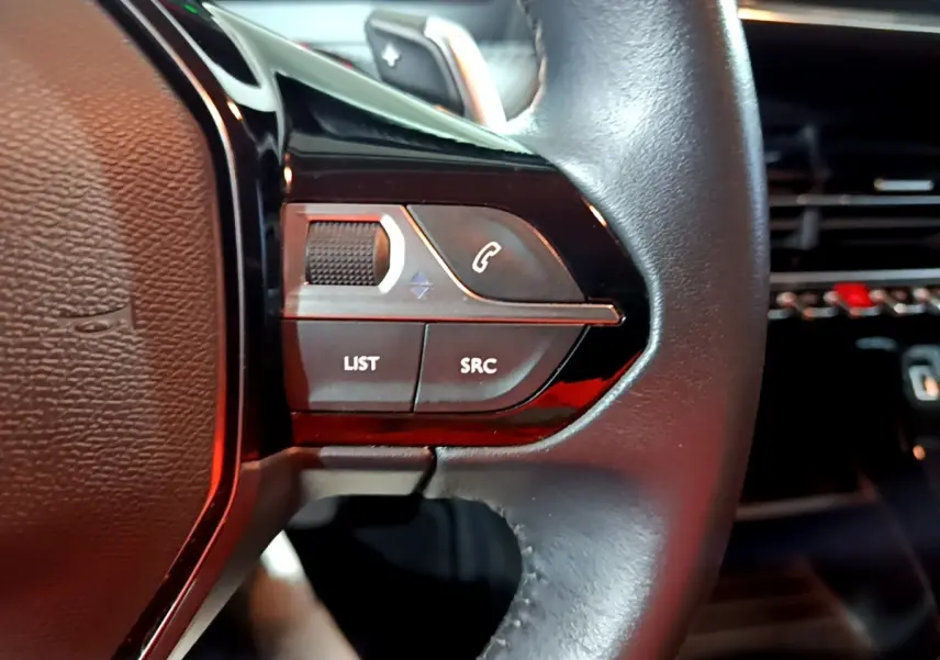 Gros plan sur le volant cuir noir multifonctions du Peugeot 2008, avec commandes audio et téléphone intégrées.