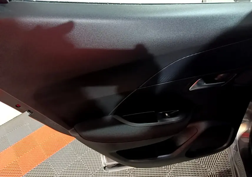 Vue intérieure du panneau de porte côté gauche du Peugeot 2008 gris clair, avec poignée argentée et commande de lève-vitre.