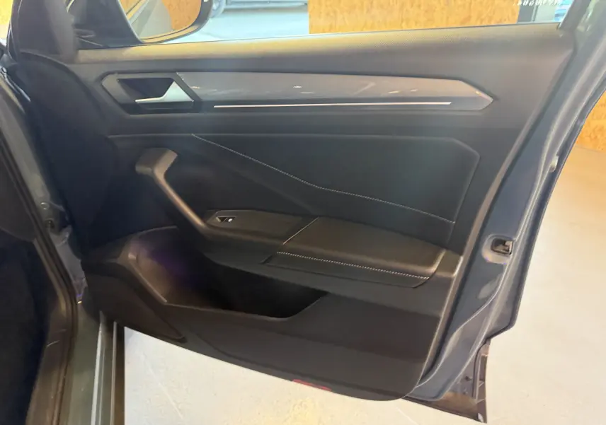 Vue intérieure de la porte avant gauche du Volkswagen T-Roc bleu 2022, avec garniture noire et surpiqûres contrastantes.
