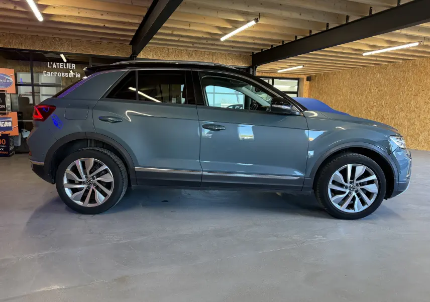 Vue de profil côté gauche d’un Volkswagen T-Roc bleu 2022 dans un garage avec jantes alliage et toit noir.