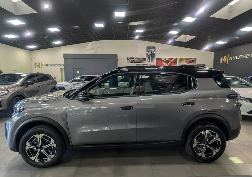 Vue de profil côté gauche d'un Citroën C3 Aircross hybride gris Mercury avec toit noir, roues à jantes bi-ton en showroom.