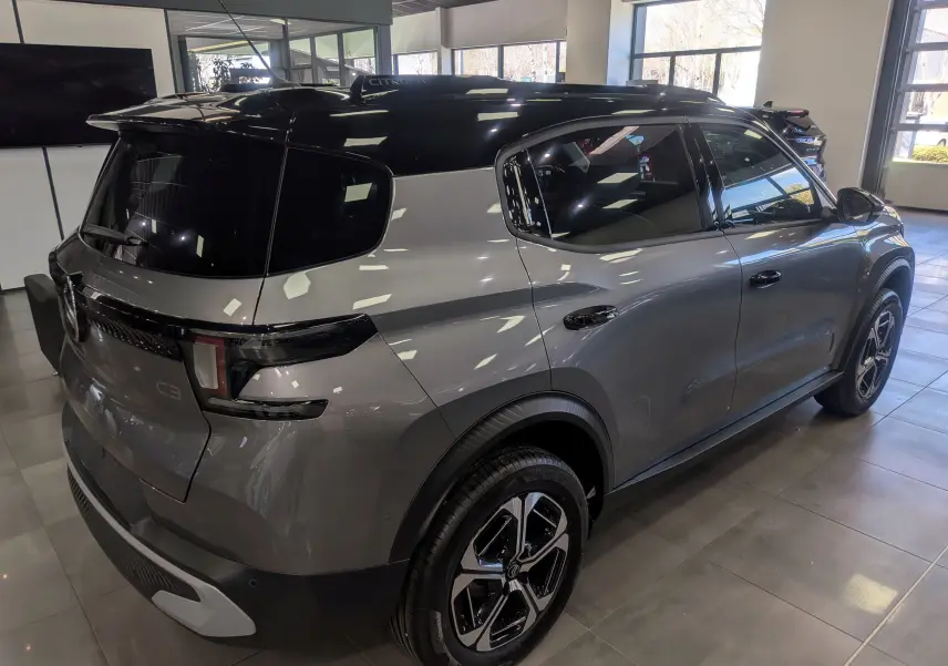 Vue 3/4 arrière droite du Citroën C3 Aircross hybride gris Mercury avec toit noir et jantes bi-ton en showroom.