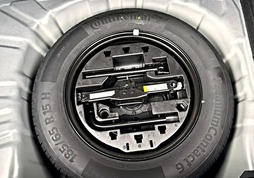 Gros plan sur la roue de secours et le kit d'outils dans le coffre d'une Renault Clio V noire.
