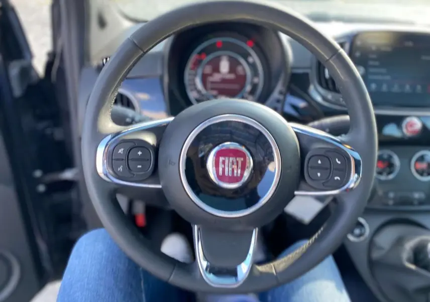 Vue centrée sur le volant noir du Fiat 500 2024 avec commandes intégrées et tableau de bord en arrière-plan.