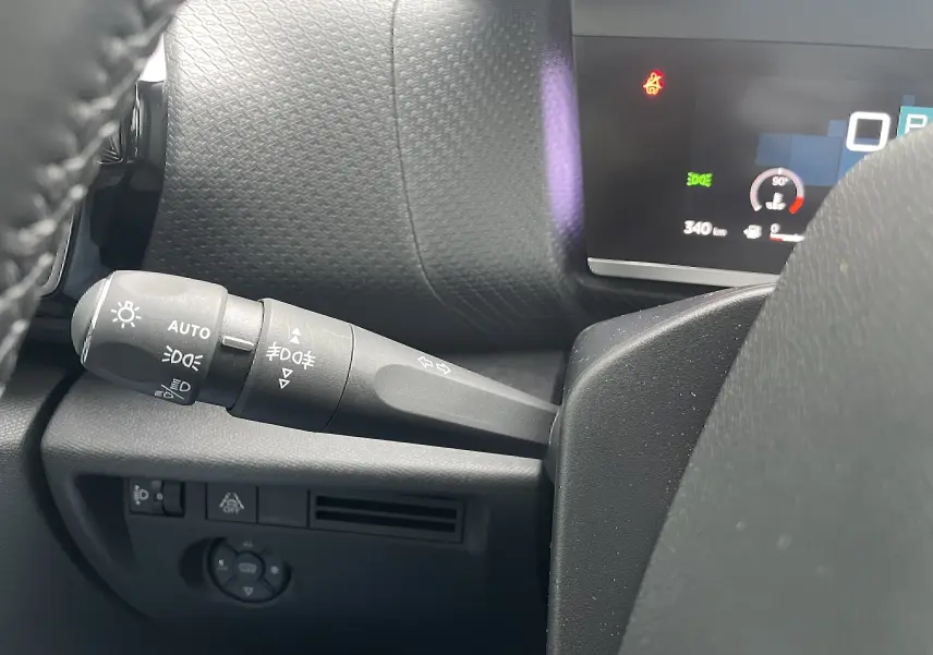 Gros plan sur la commande des phares et clignotants à gauche du volant dans l’habitacle gris-noir d’une Citroën C4 blanche 2022.