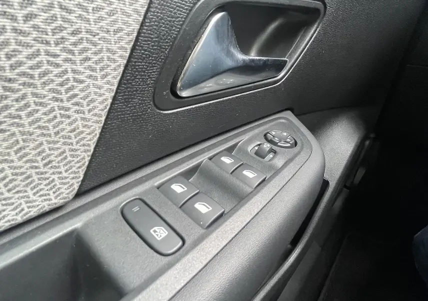 Gros plan sur la commande des vitres et le bouton de réglage des rétroviseurs côté conducteur, intérieur tissu gris noir.