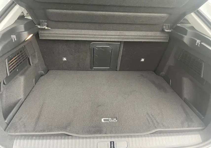 Coffre ouvert vu de l'arrière d'une Citroën C4 blanche, tapis noir avec logo C4 et éclairage intérieur.