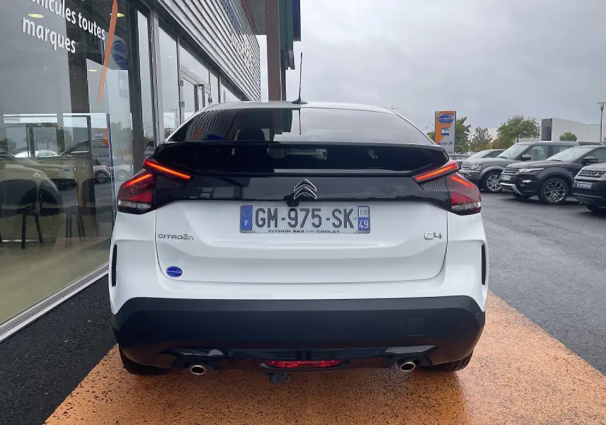 Vue arrière d'une Citroën C4 blanche 2022 avec feux LED allumés et toit noir brillant sur parking humide.