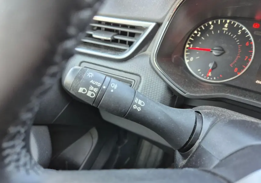 Gros plan sur la commande des phares et clignotants à gauche du volant dans une Renault Clio noire, tableau de bord visible.