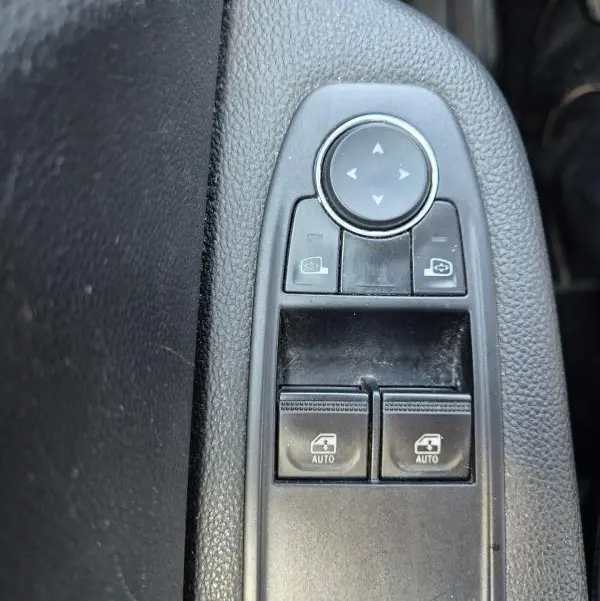 Gros plan sur les commandes de réglage des rétroviseurs et des vitres électriques côté conducteur d’une Renault Clio noire.