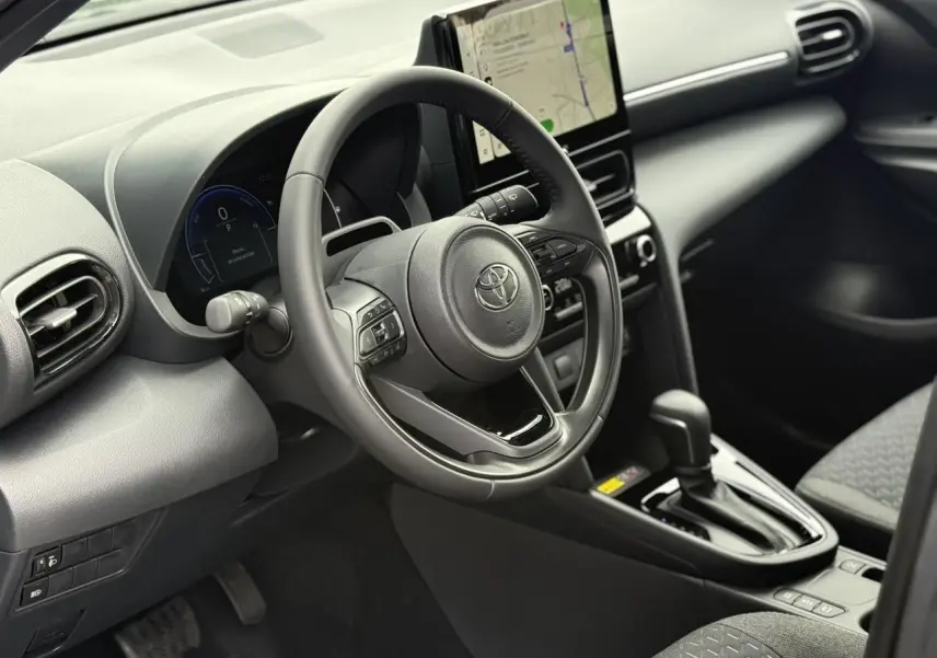 Vue intérieure côté conducteur de la Toyota Yaris Cross 2026, volant cuir, écran tactile vertical et levier de boîte auto.