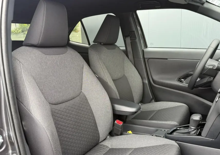 Vue intérieure côté droit montrant les sièges avant gris tissu avec accoudoir central et levier de boîte automatique Toyota Yaris Cross.