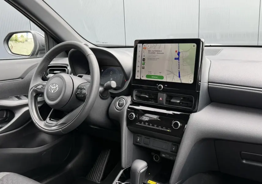 Vue intérieure côté conducteur de la Toyota Yaris Cross gris Atlas, avec écran tactile central et volant cuir.