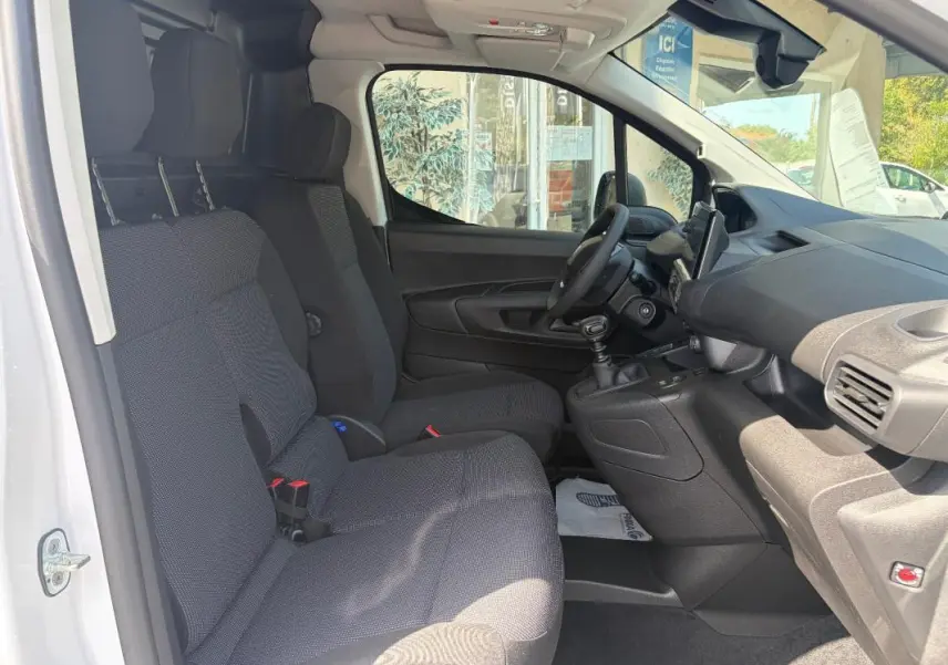 Vue intérieure côté conducteur du Peugeot Partner blanc 2026, montrant sièges tissu, volant multifonctions et tableau de bord avec GPS tactile.