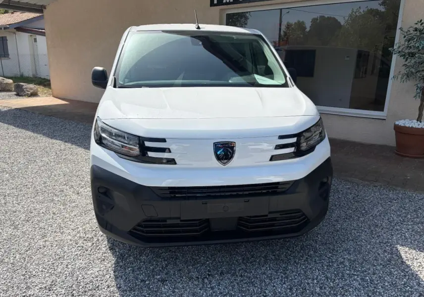 Vue frontale d’un Peugeot Partner blanc 2026 avec calandre noire et logo Peugeot central bien visible.