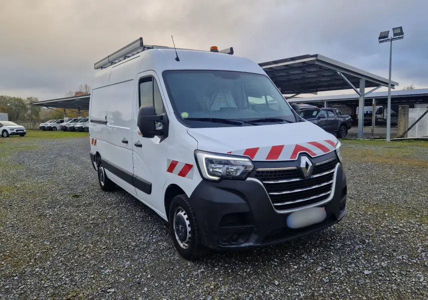 Renault Master blanc en 3/4 avant droit avec bandes rouges réfléchissantes et galerie sur le toit.