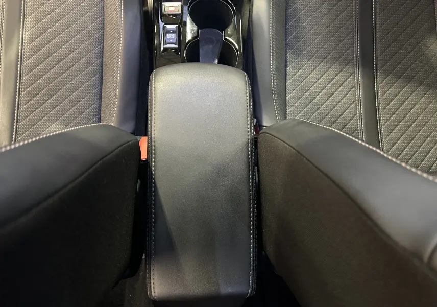 Vue plongeante sur l'accoudoir central et les sièges avant en tissu noir du Peugeot 2008 Allure Hybrid 2025.