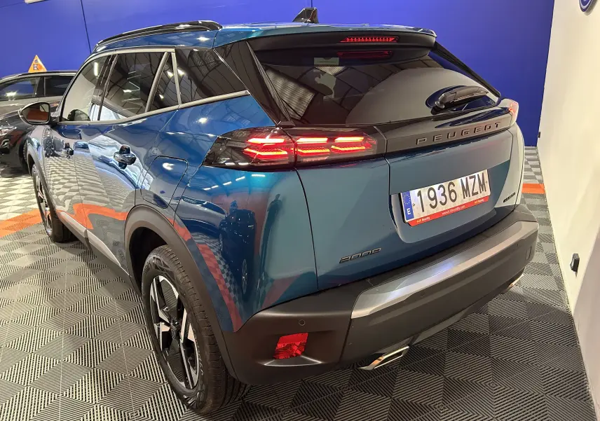 Vue 3/4 arrière droite d’un Peugeot 2008 Allure Hybrid 145 bleu Obsession avec feux arrière allumés en intérieur.