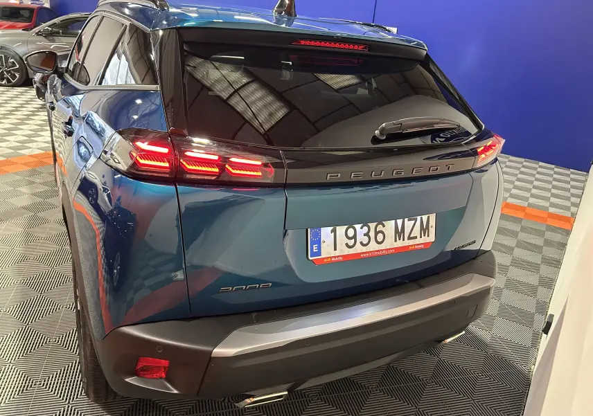 Vue 3/4 arrière d’un Peugeot 2008 Allure Hybrid 145 bleu Obsession avec feux arrière allumés et toit noir brillant.