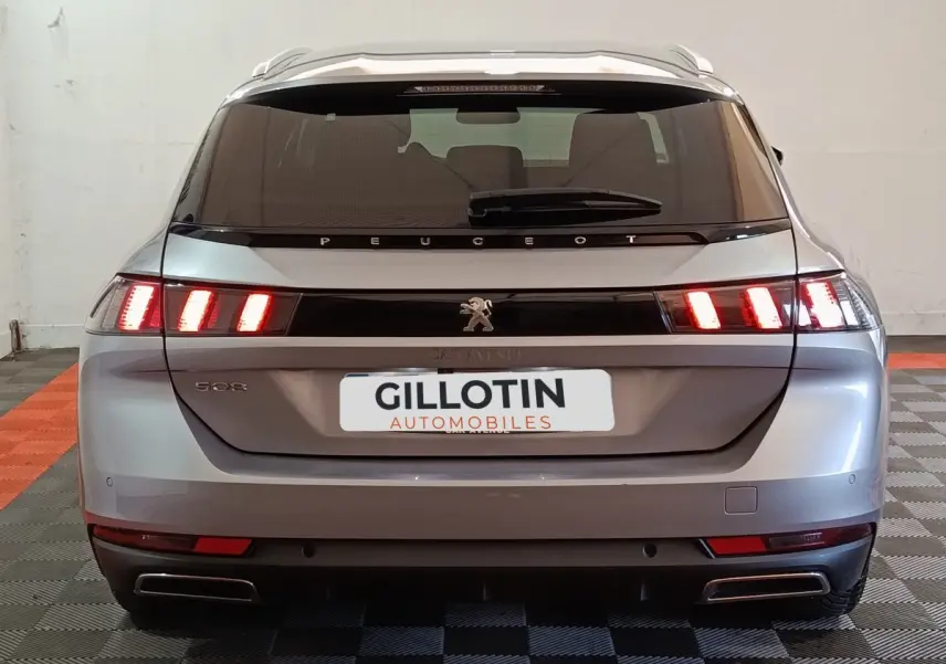 Vue arrière d'une Peugeot 508 gris clair avec feux LED allumés dans un intérieur de garage.