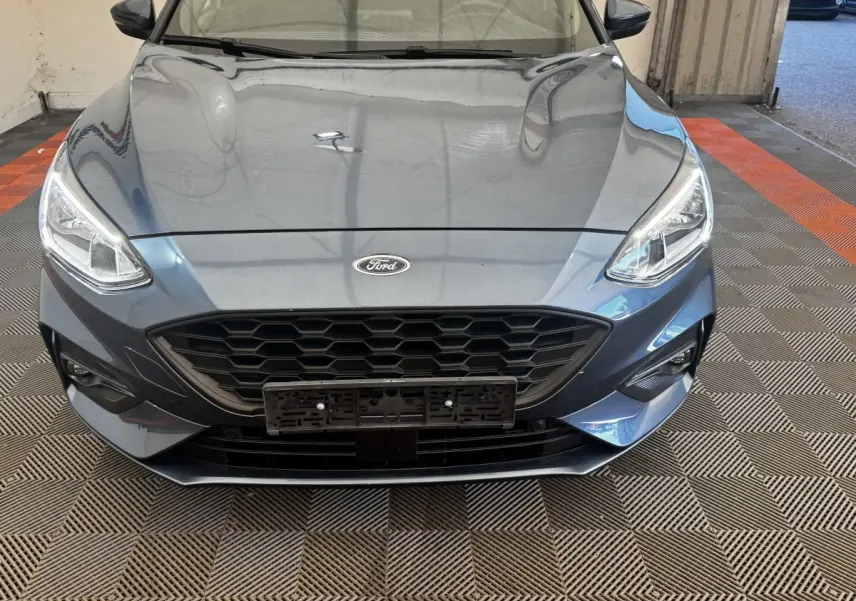 Vue avant rapprochée d'une Ford Focus 5P St-Line bleu métallisé, mettant en valeur sa calandre hexagonale et ses phares LED.