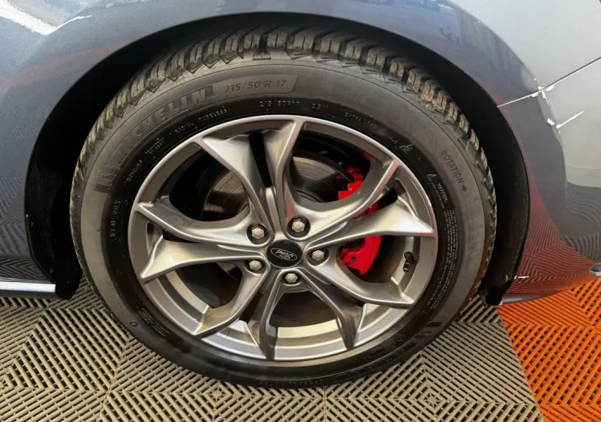 Gros plan sur la roue avant droite d'une Ford Focus bleu, avec jante alliage et étrier de frein rouge visible.