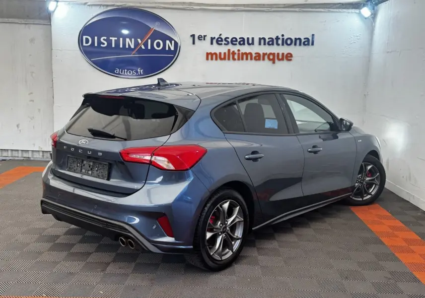 Vue 3/4 arrière droite d'une Ford Focus bleu métallisé avec jantes alliage et double sortie d'échappement sportive.