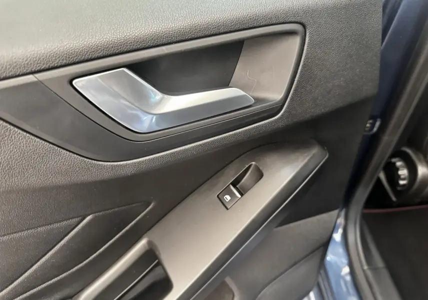 Gros plan sur la poignée intérieure et le bouton de lève-vitre côté conducteur d'une Ford Focus bleu 5 portes.