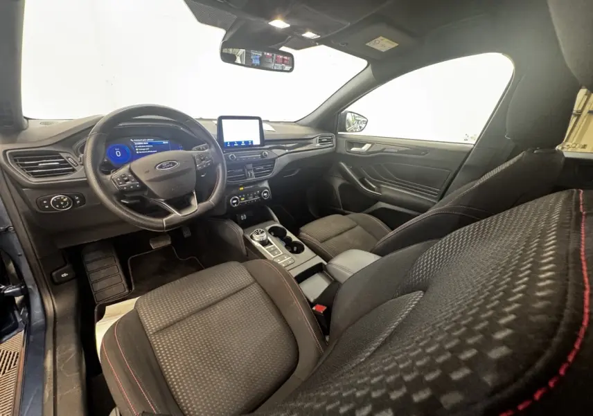 Vue intérieure côté conducteur de la Ford Focus St-Line 2022, sièges noirs avec surpiqûres rouges et écran tactile central.