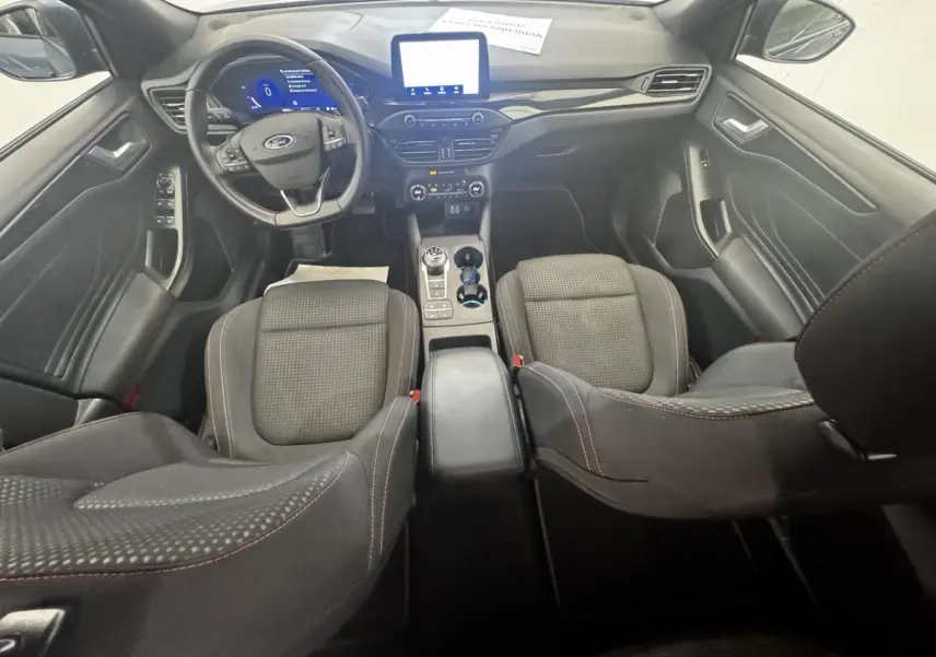 Vue intérieure avant de la Ford Focus 5P St-Line 2022, sièges noirs avec surpiqûres rouges et tableau de bord numérique.