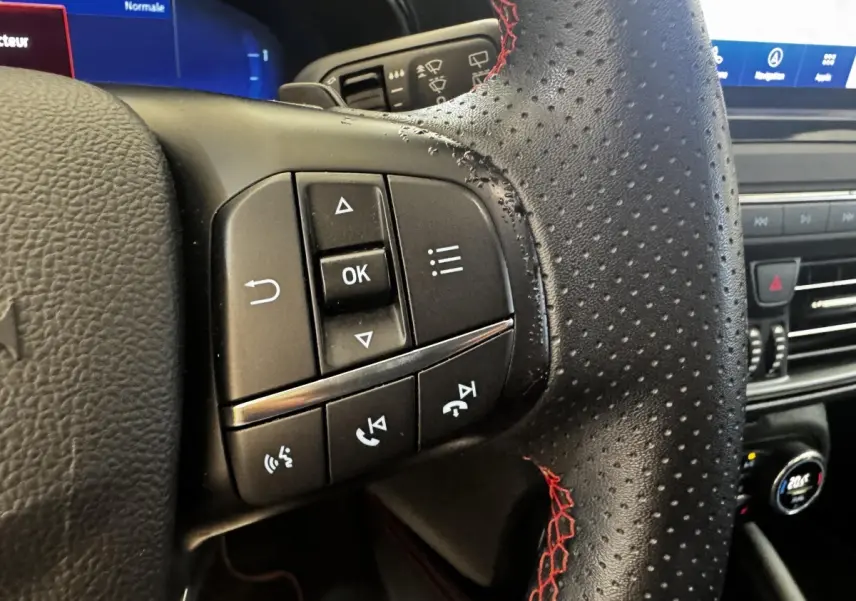 Gros plan sur les commandes gauche du volant en cuir noir perforé avec surpiqûres rouges de la Ford Focus bleu 2022.