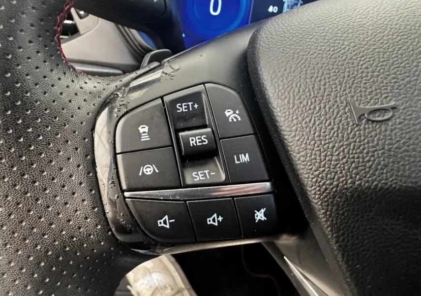 Gros plan sur les commandes multifonctions à gauche du volant cuir perforé d'une Ford Focus bleu 2022.