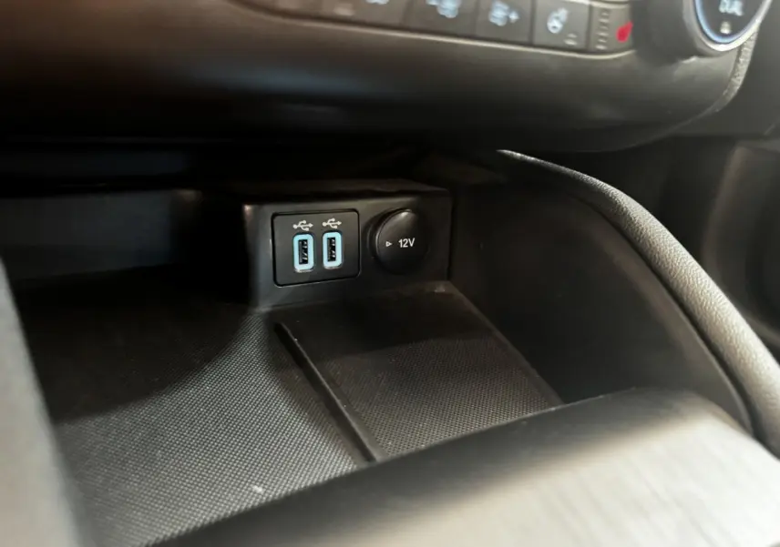 Gros plan sur la console centrale noire de la Ford Focus 5P avec prises USB doubles et prise 12V visible.
