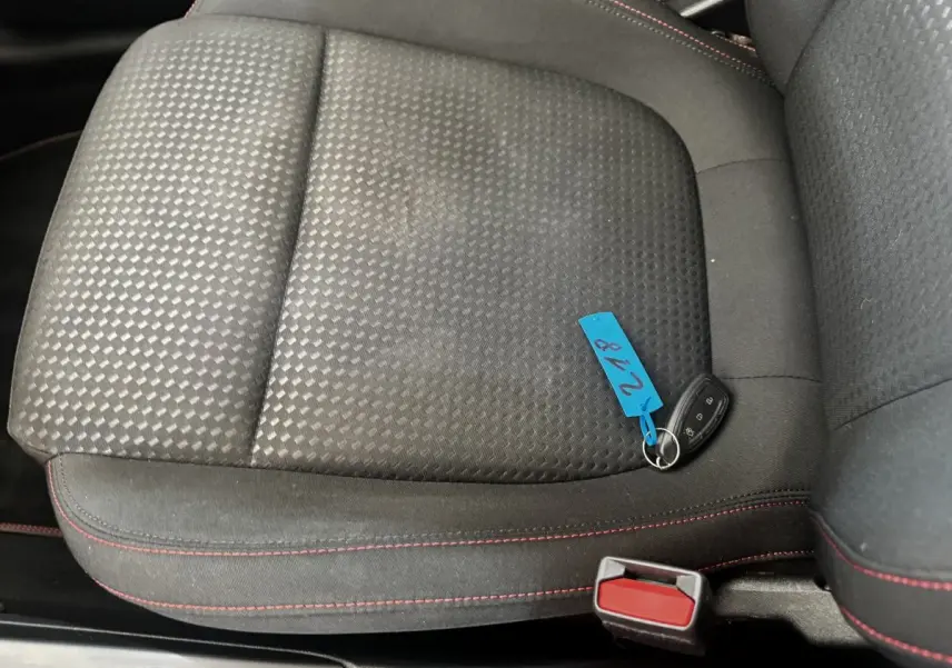 Gros plan sur le siège avant droit en tissu noir avec surpiqûres rouges et clé de voiture Ford posée dessus.