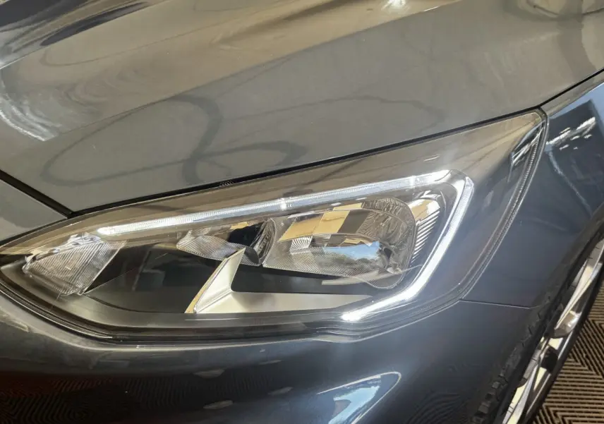 Gros plan sur le phare avant droit de la Ford Focus 5P bleu métallisé, soulignant ses détails LED modernes.