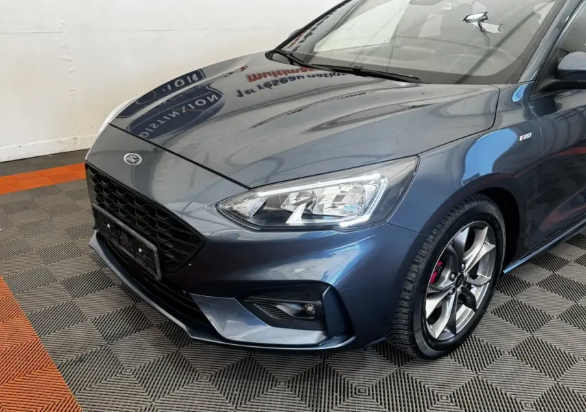 Vue 3/4 avant droit d'une Ford Focus St-Line bleue avec phares LED et jantes alliage sport visibles.