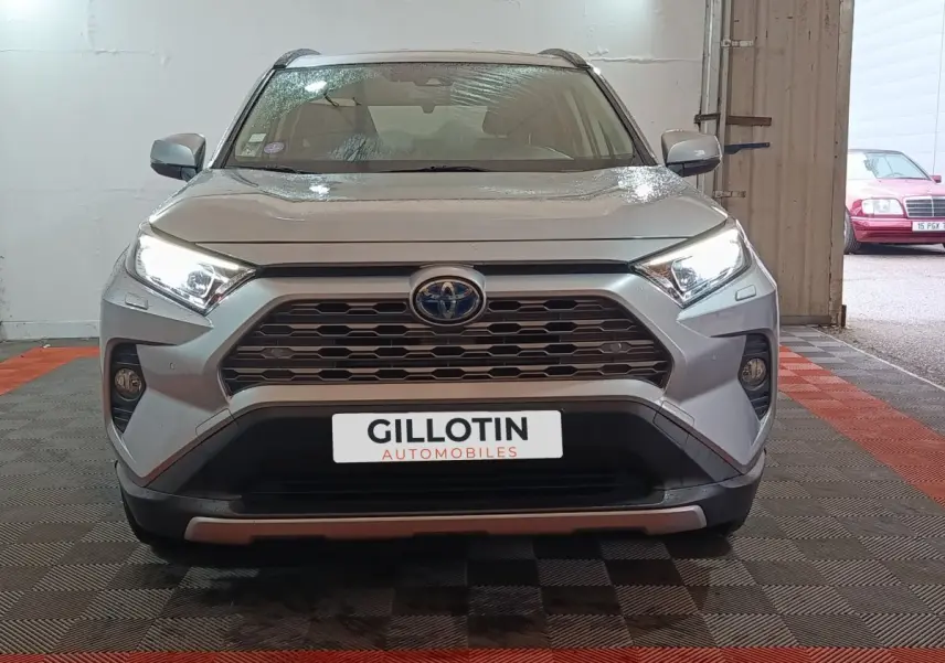 Vue frontale du Toyota RAV4 hybride gris clair avec calandre hexagonale et feux LED allumés dans un garage.