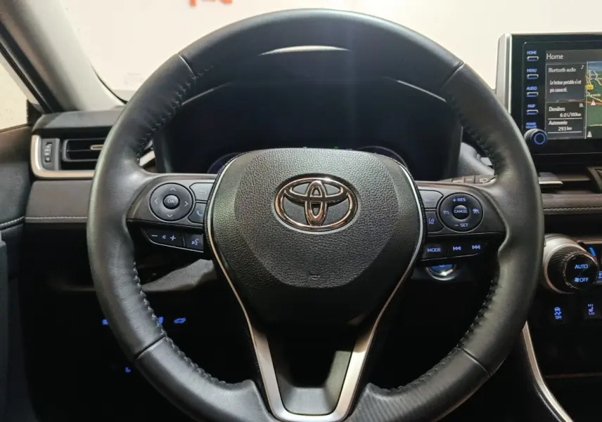 Vue rapprochée du volant cuir noir du Toyota RAV4 hybride 2021 avec commandes multifonctions et tableau de bord digital.