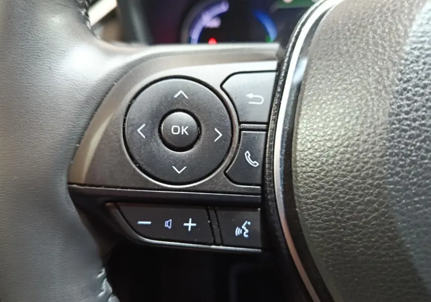 Gros plan sur les commandes multifonctions noires à gauche du volant cuir du Toyota RAV4 hybride 2021.